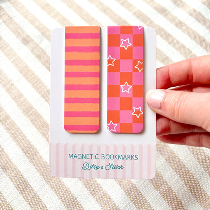 Two colourful magnetic bookmarks on a card held by a hand against a striped background